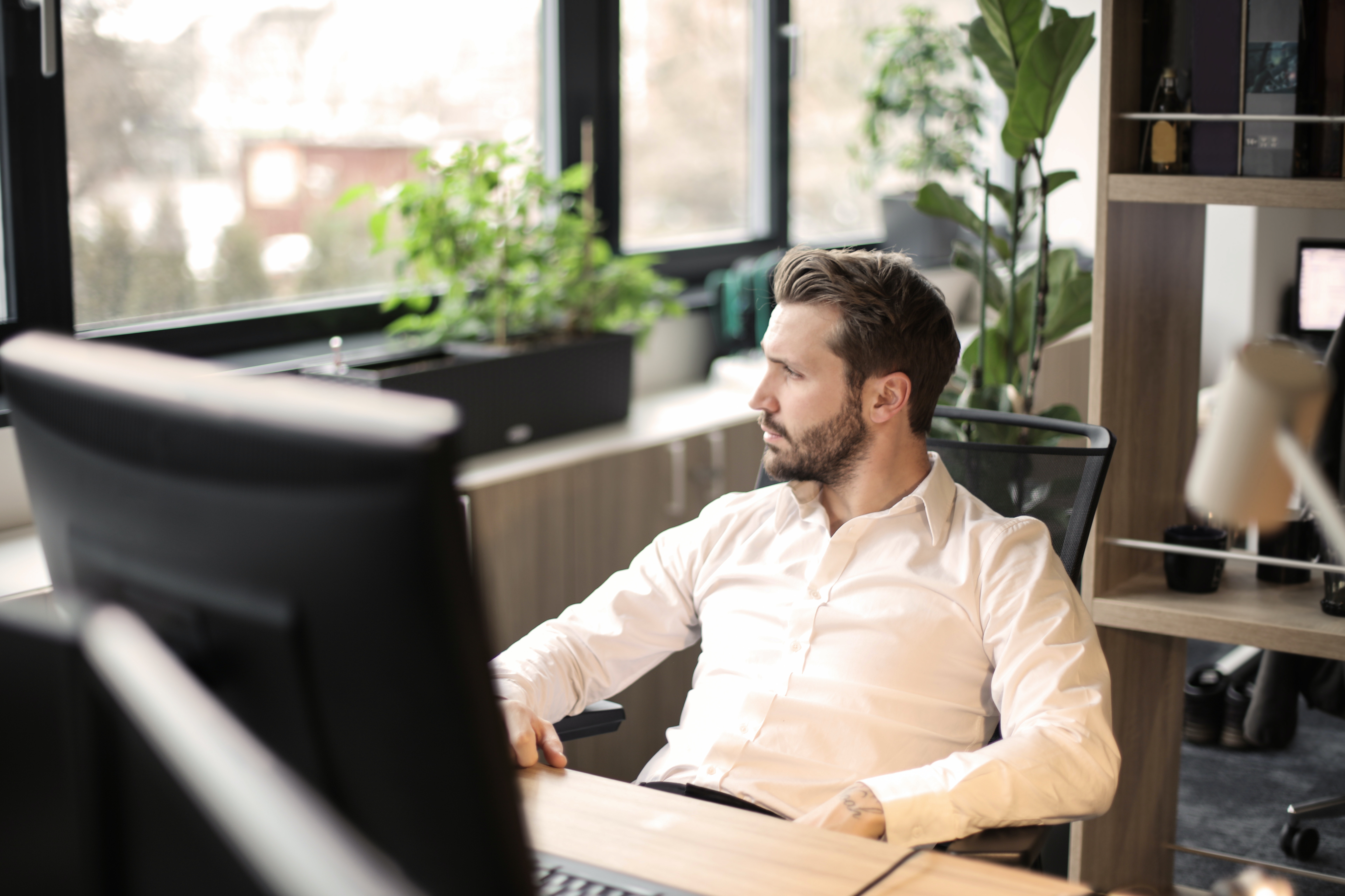 A man sitting behind a computer on a desk looking at his right side thinking
